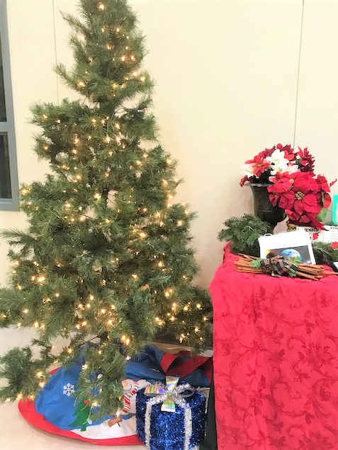 Photo of a Christmas tree with lights next to a table with a red tablecloth and a poinsettia.