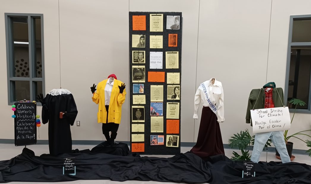 Photo of display for Women's History Month featuring four mannequins wearing women's clothing through the years and a large display board with facts about women throughout history.