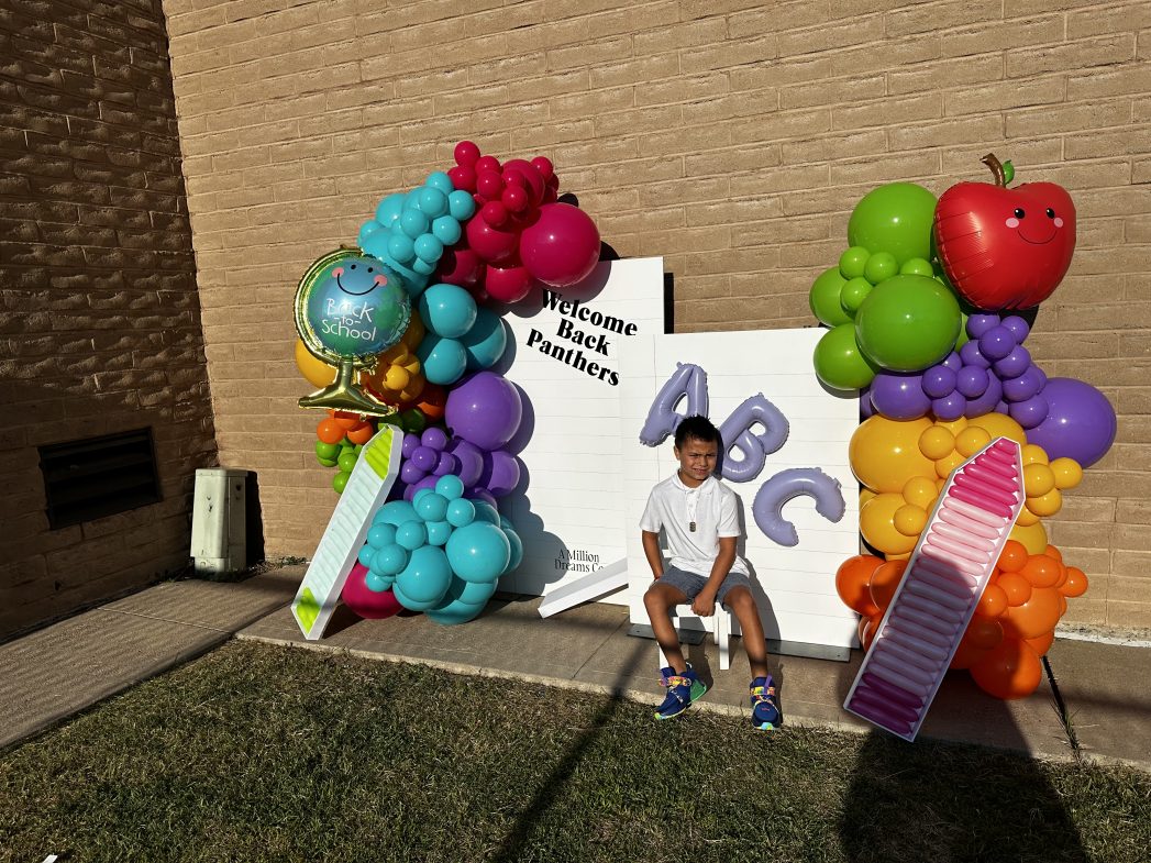 Photo of student underneath a banner of balloons on the first day of school