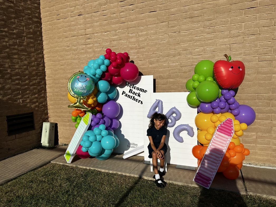 Photo of student underneath a banner of balloons on the first day of school