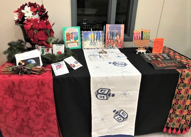 Photo of display a table with red and black tablecloths featuring a holiday display with information on Hanukkah and the origin of the poinsettia.