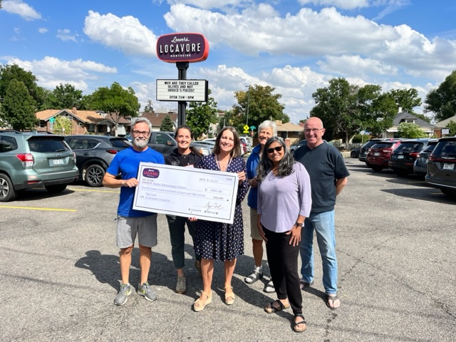 Photo of 6 people holding a giant check in a parking lot in front of a sign for Leevers Locavore.