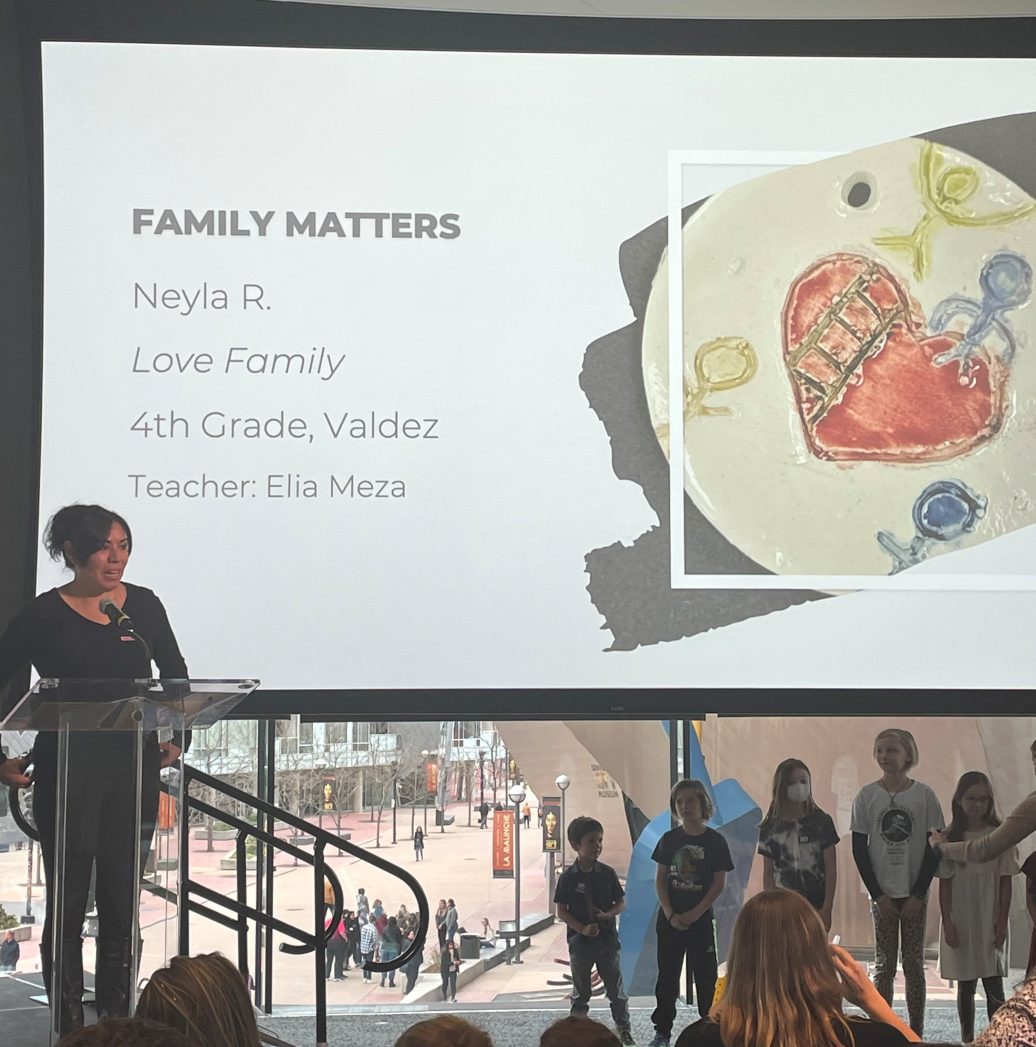 Art teacher, Ms. Meza, standing at a podium in front of a projection screen.