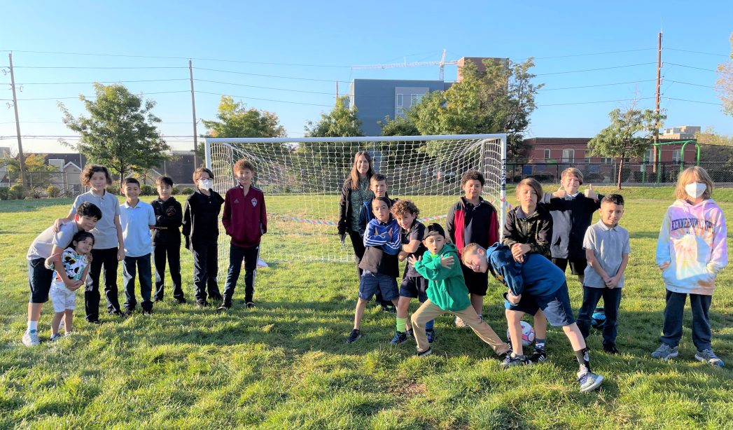 Photo of students and principal in front of a new soccer goal on green grass.