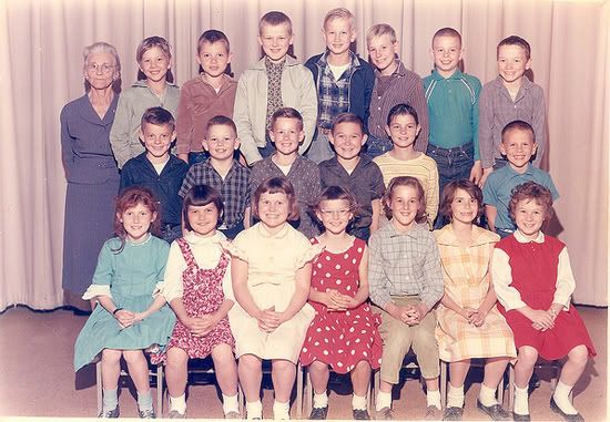 Vintage classroom photo of students and teacher against a background of a beige curtain.
