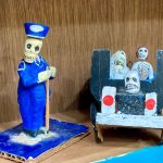Close up of Day of the Dead skeleton figurines, one wearing a blue suit and two riding in a car.