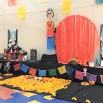 Day of the Dead ofrenda with statue of Frida Kahlo and a Mexican brightly colored flag banner. Yellow marigolds are on the floor.